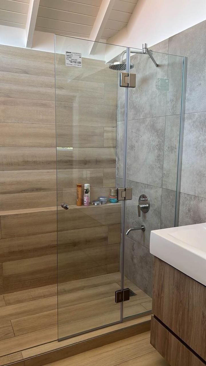 Ducha con puerta de cristal, azulejos con aspecto de madera y grifería de acero inoxidable en un baño.