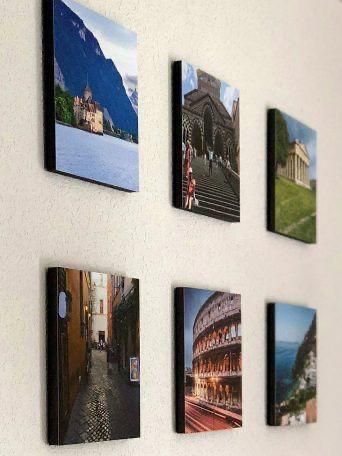 Lienzos impresos con fotografías de viajes montados sobre una pared blanca; incluye escenas de montaña, edificios y calles.