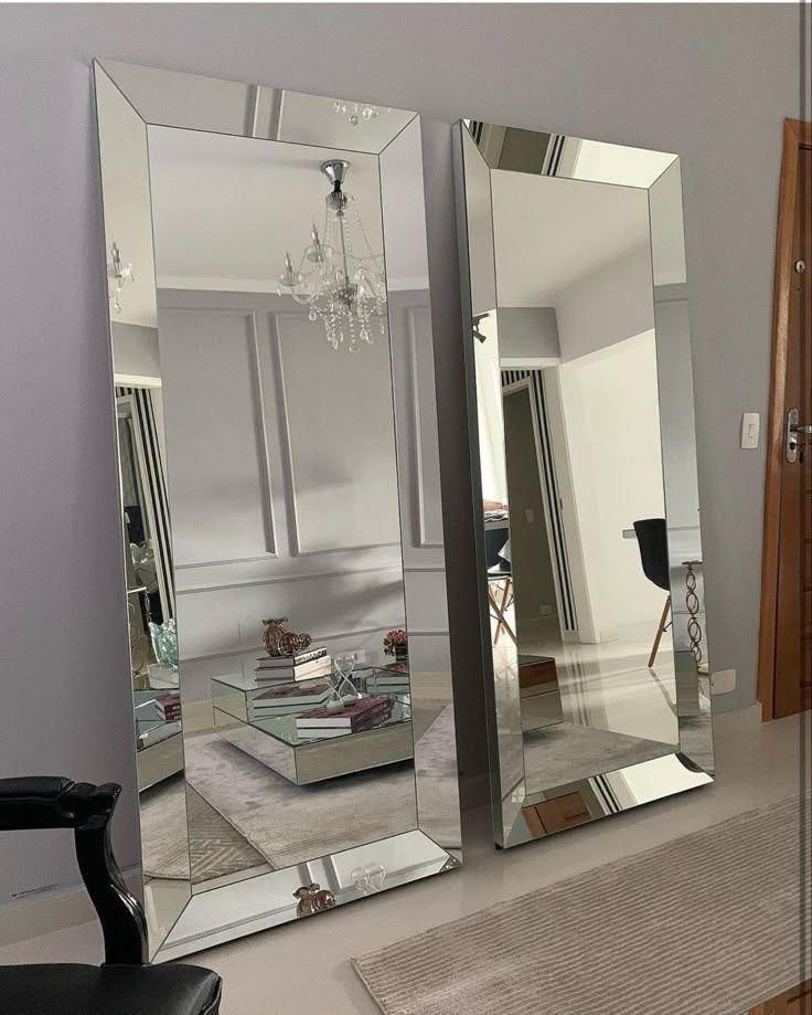 Dos grandes rectángulos espejados apoyados contra una pared gris reflejan una sala de estar con muebles.