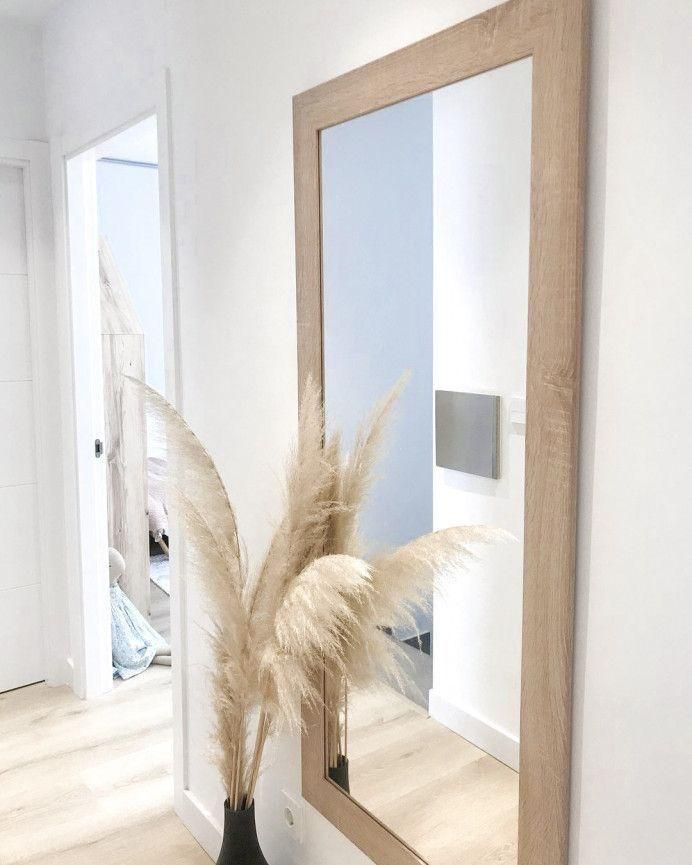 Espejo grande con marco marrón claro, junto a hierba de la pampa seca en un jarrón negro, interior de un pasillo.