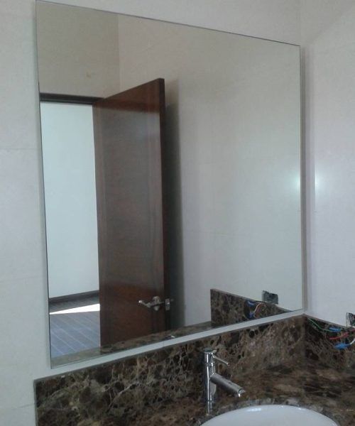 Gran espejo rectangular sobre la encimera del baño, que refleja una puerta.