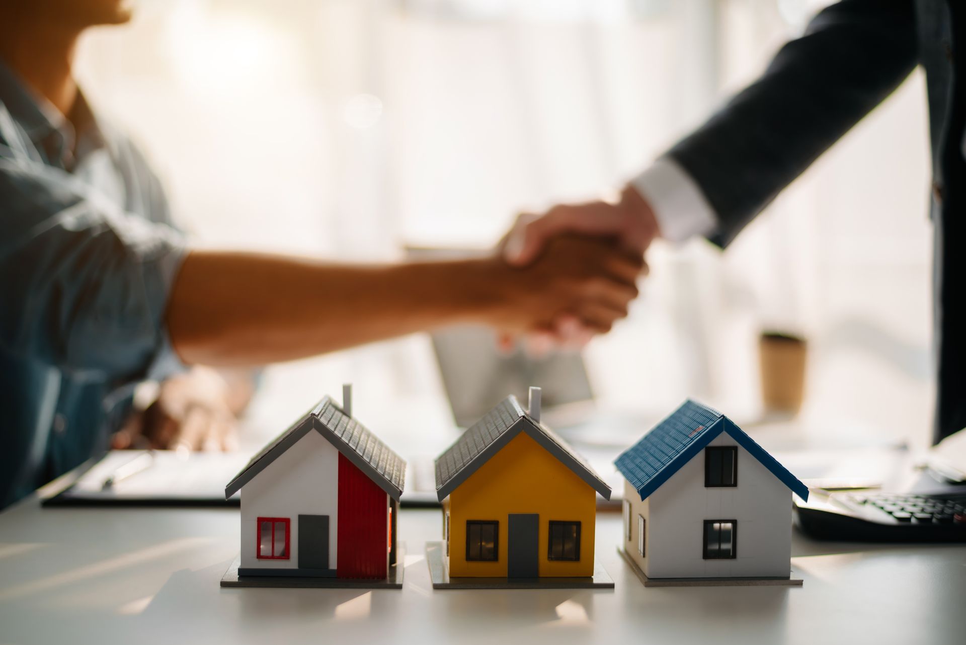 A man and a woman are shaking hands over a table with three small houses.