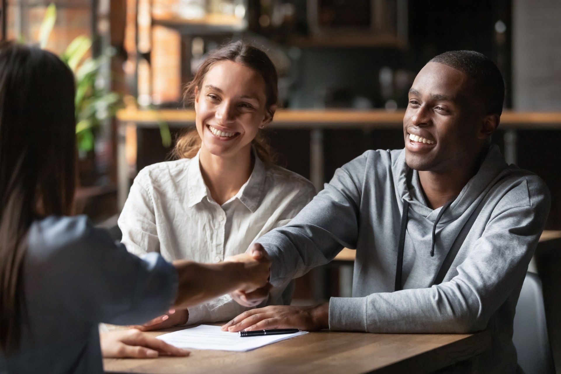 A man and a woman are shaking hands while sitting at a table.