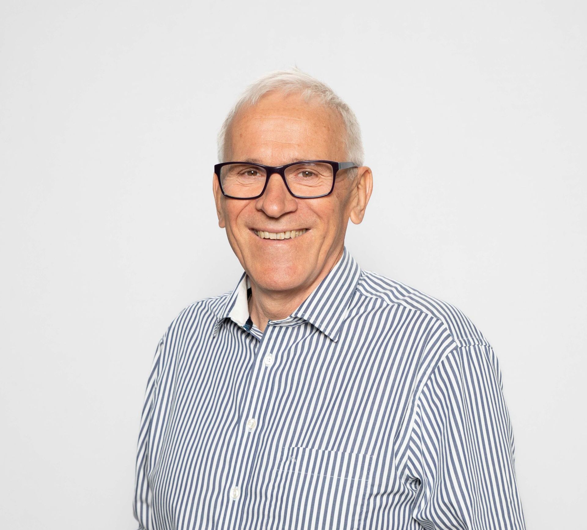 Ein Mann mit Brille und gestreiftem Hemd lächelt in die Kamera.