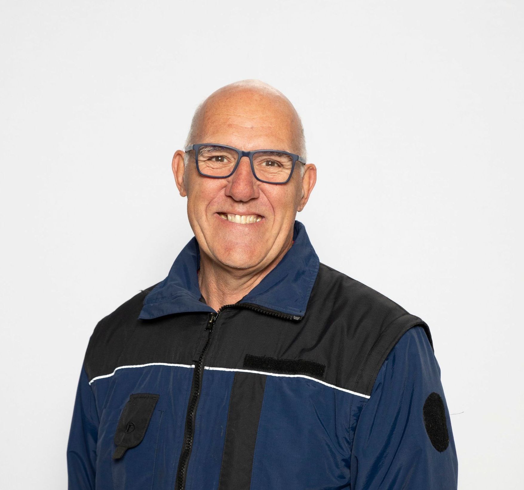 Ein Mann mit Brille und blauer Jacke lächelt in die Kamera.