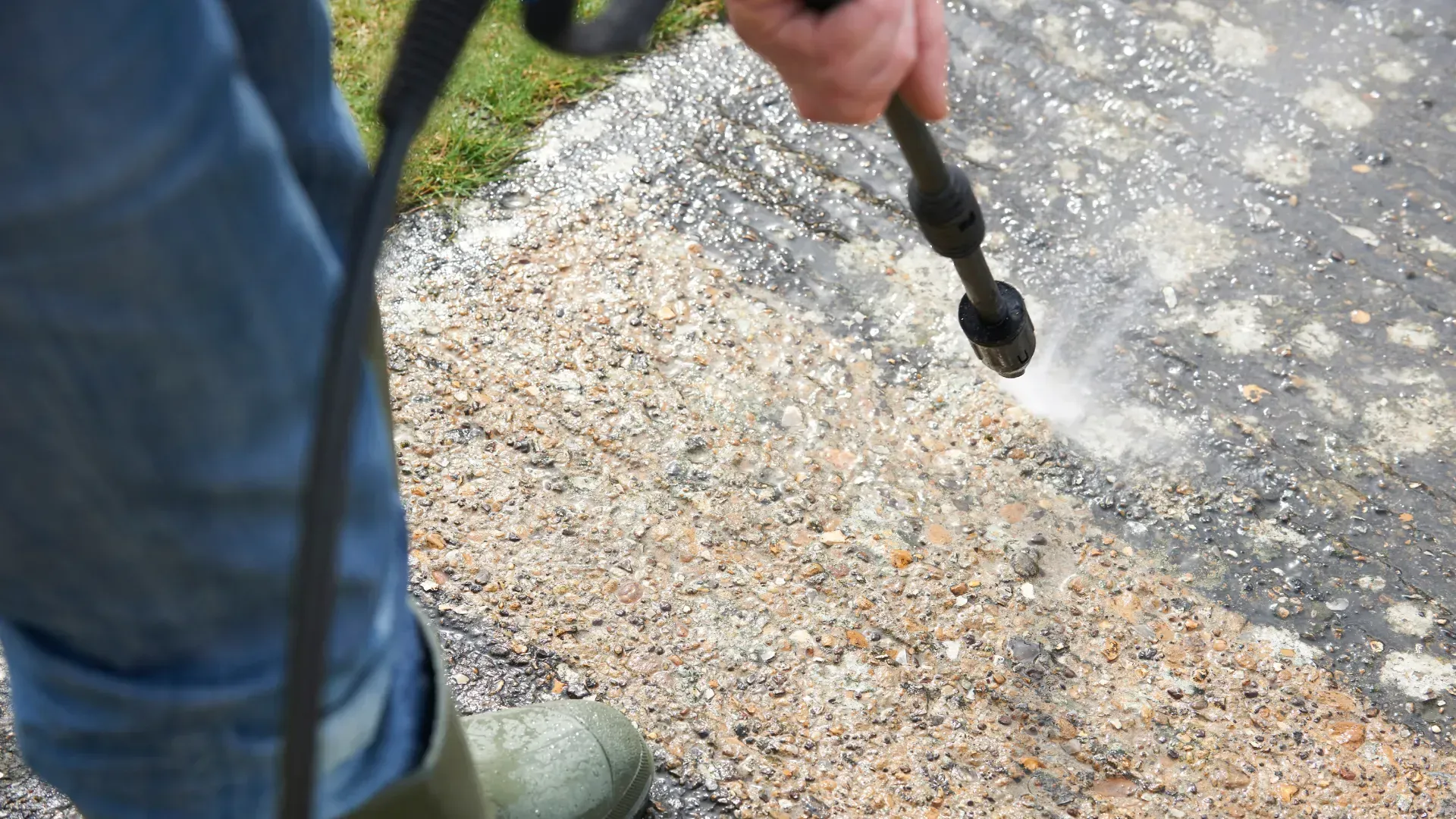 A person is using a high pressure washer to clean a sidewalk.