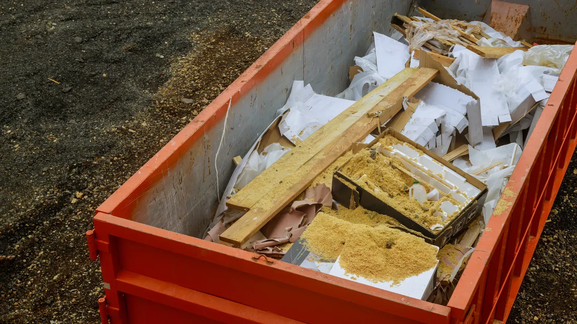 A large orange dumpster filled with wood and paper.