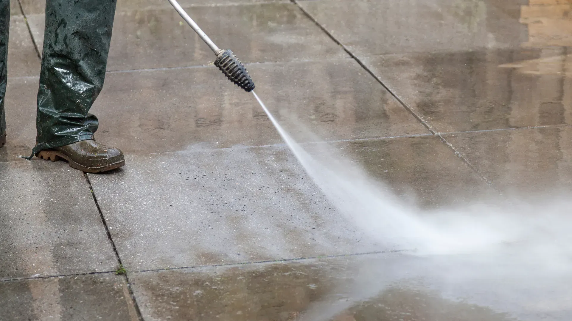 A person is using a high pressure washer to clean a concrete floor.