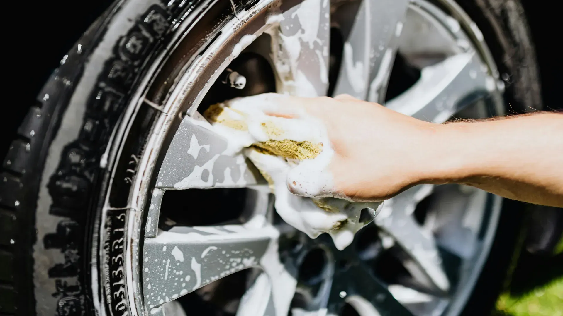 A person is washing a car wheel with a sponge.