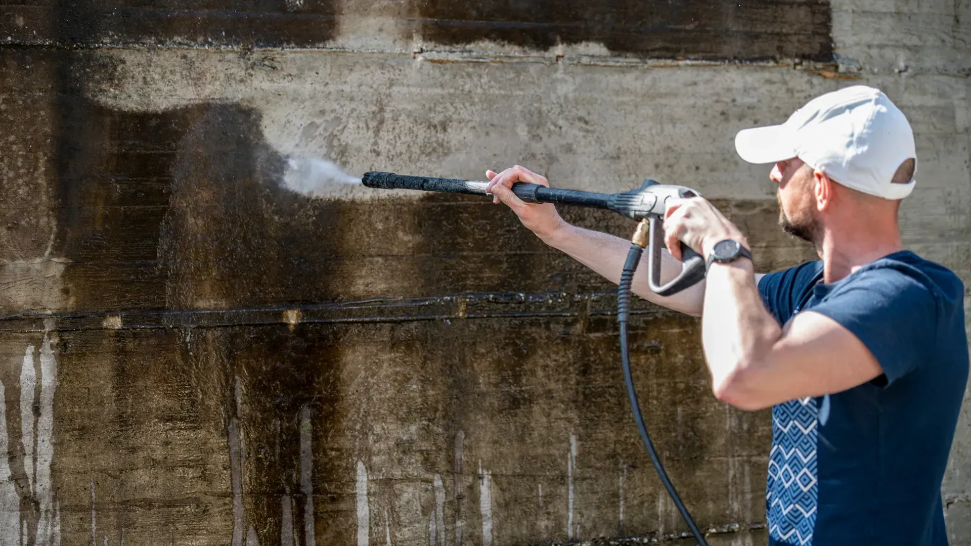 A man is using a high pressure washer to clean a wall.