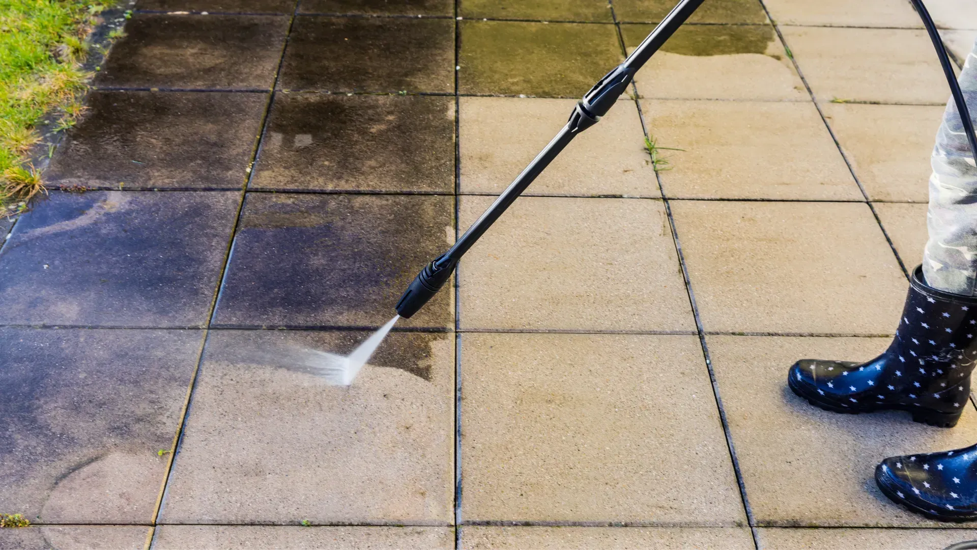 A person is cleaning a sidewalk with a high pressure washer.