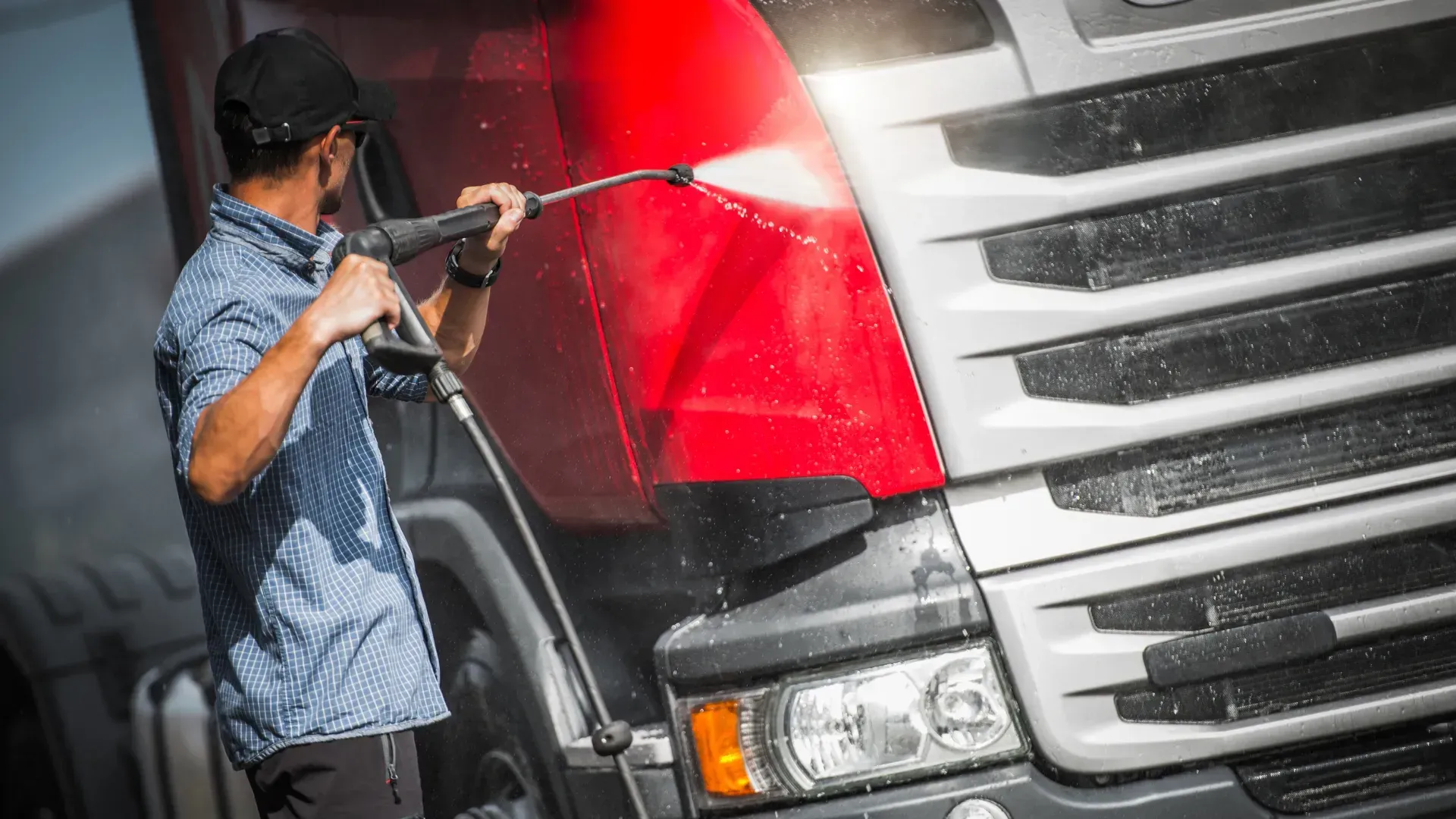 A man is washing a truck with a high pressure washer.