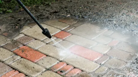 A person is using a high pressure washer to clean a brick walkway.