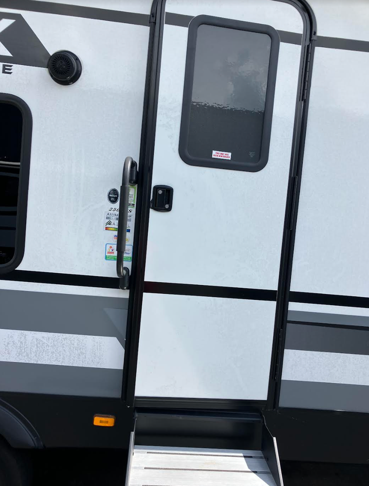 RV door with steps and handrail; the door is white with a window and black trim.