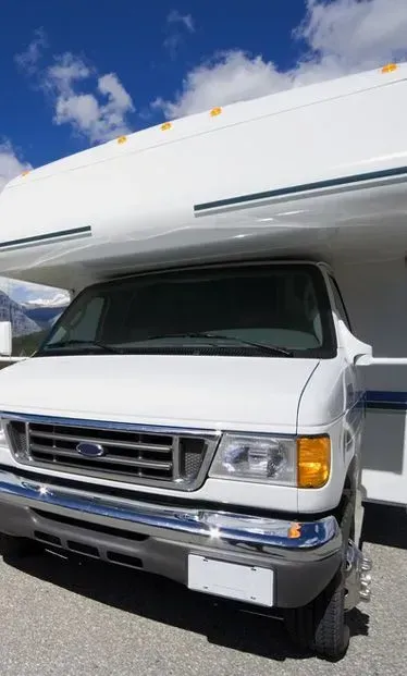 White campervan parked on a road against a backdrop of blue sky and mountains.