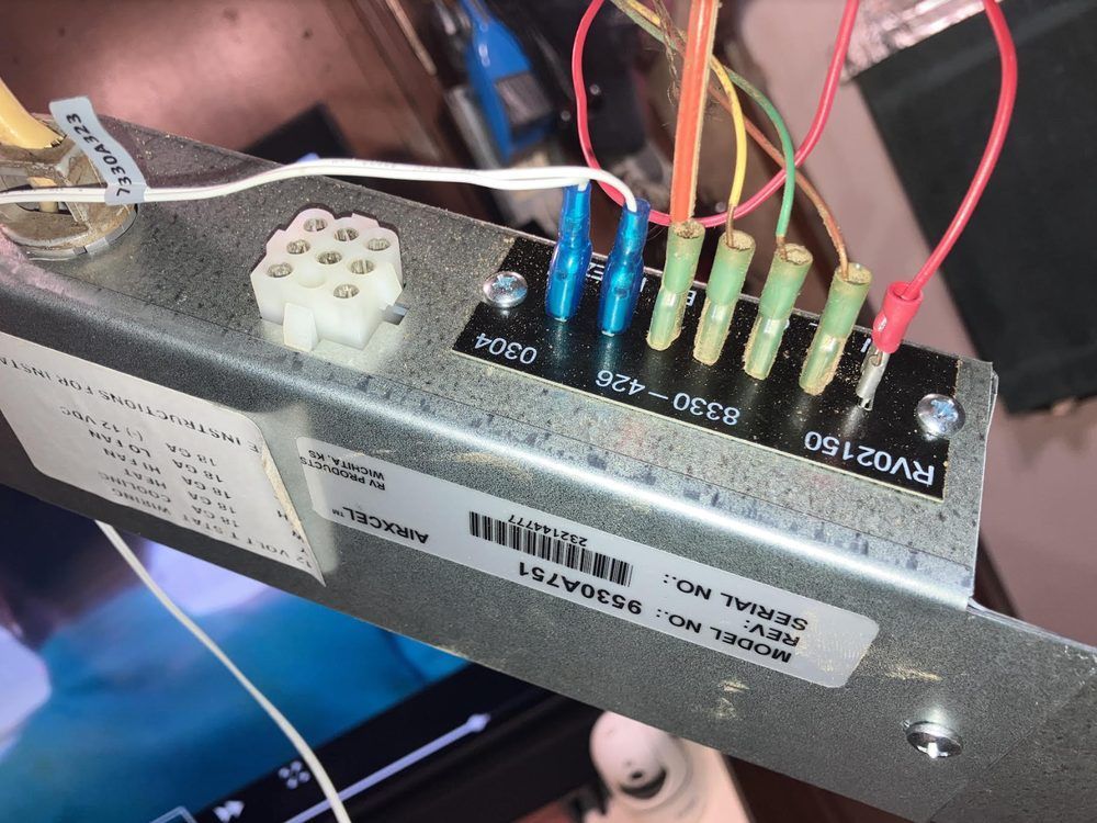 Close-up of a metal component with labeled wire connectors, a tube socket, and a serial number sticker. Wires are red, yellow, green, blue, and white.