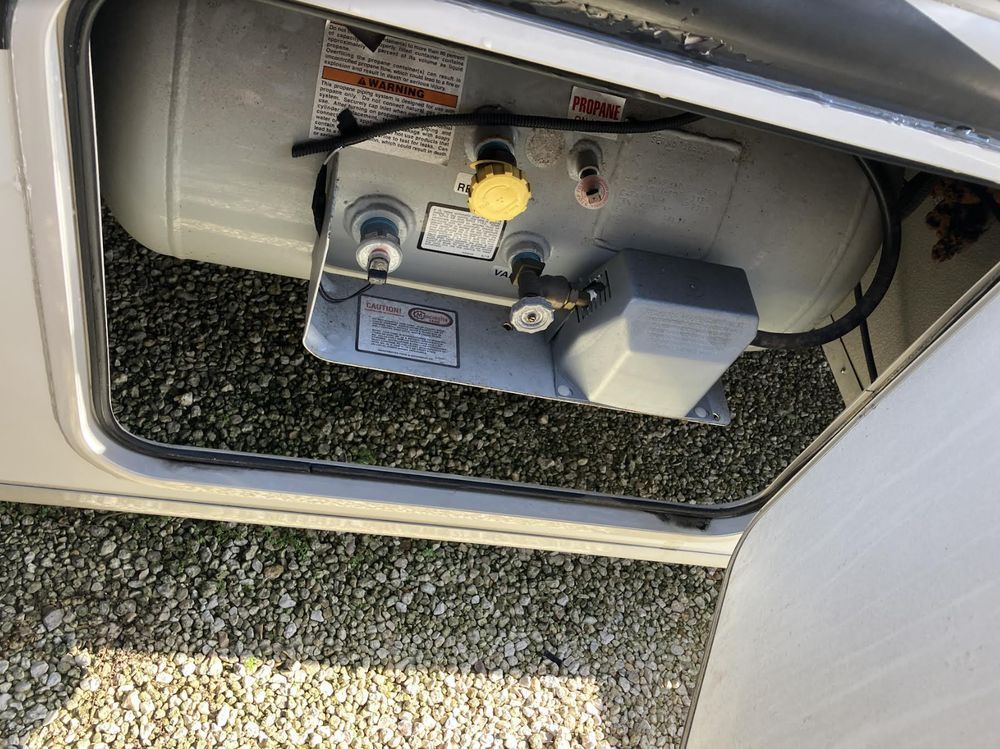 A compartment containing two propane tanks in a recreational vehicle. The tanks are gray, and the compartment door is open.