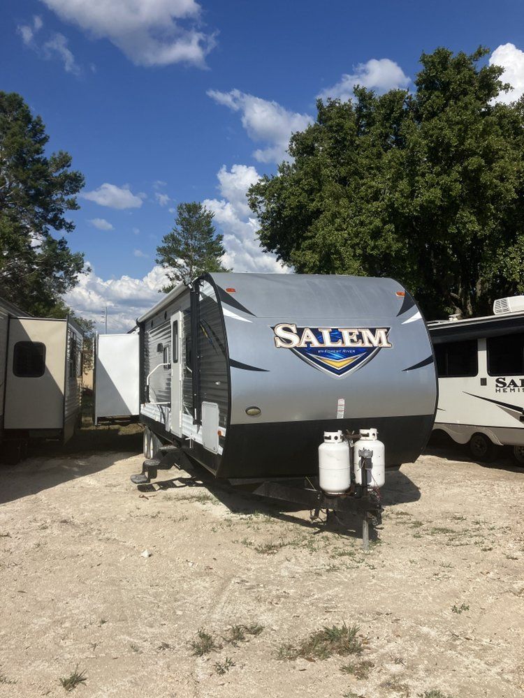 A Salem travel trailer parked on gravel under a blue sky. White propane tanks are visible.