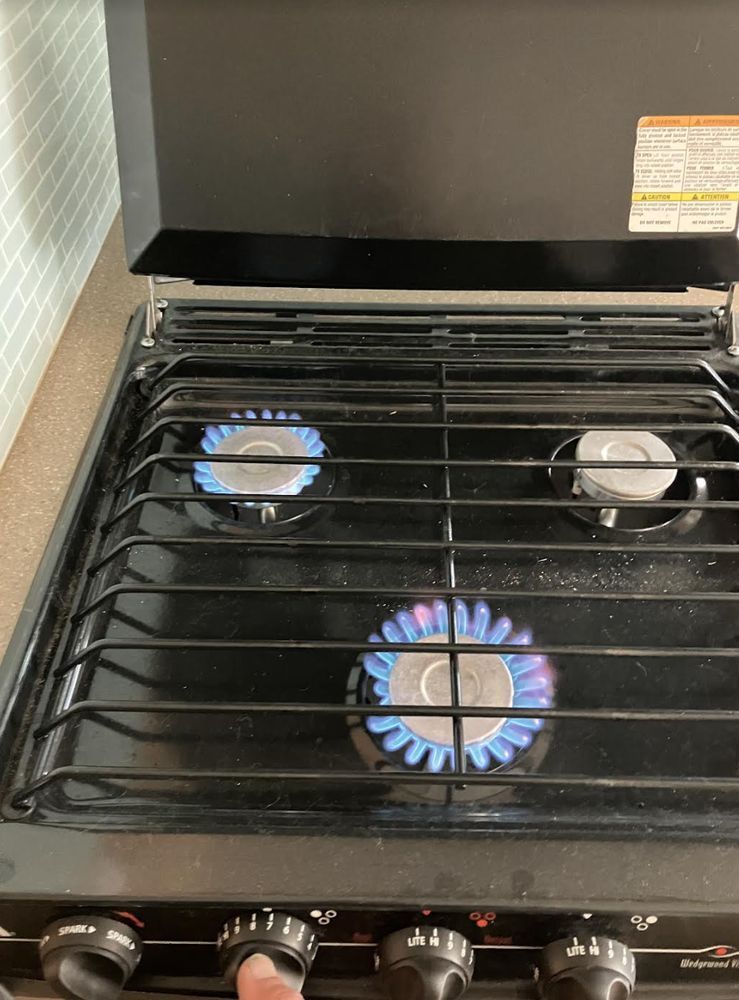 A gas stovetop with three burners lit with blue flames. A hand is turning a knob.