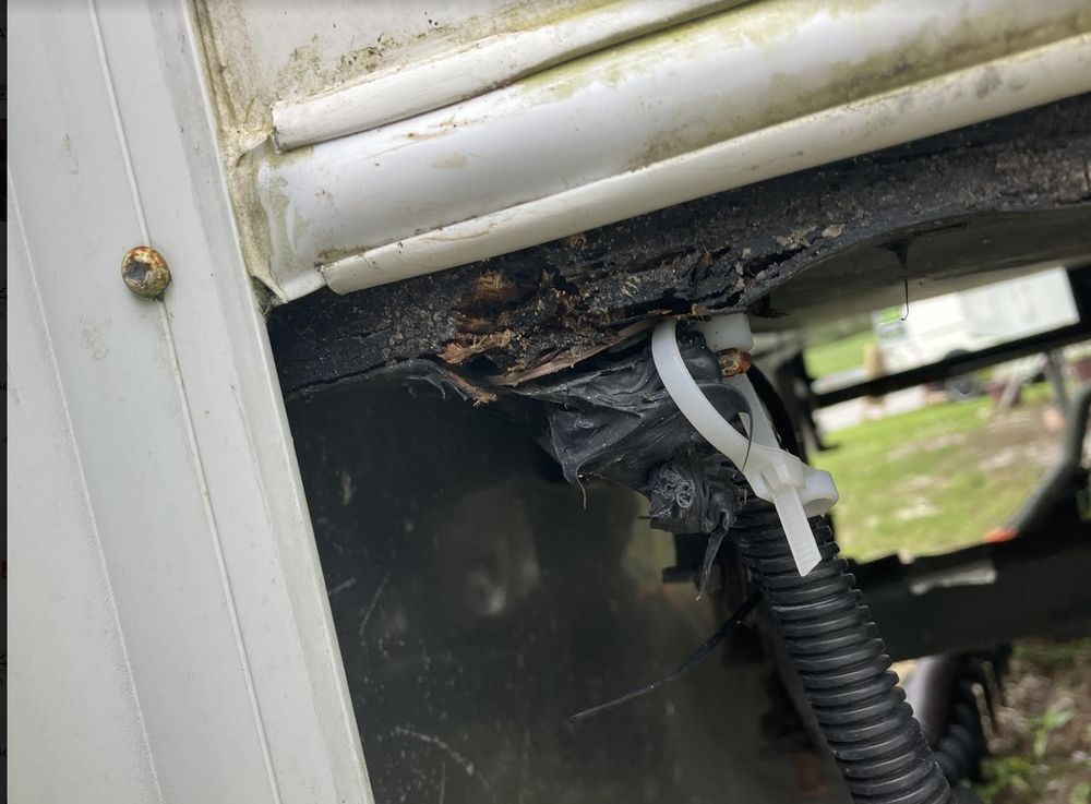Severely rotted underside of a white RV with a black undercarriage, revealing structural damage and corroded metal.