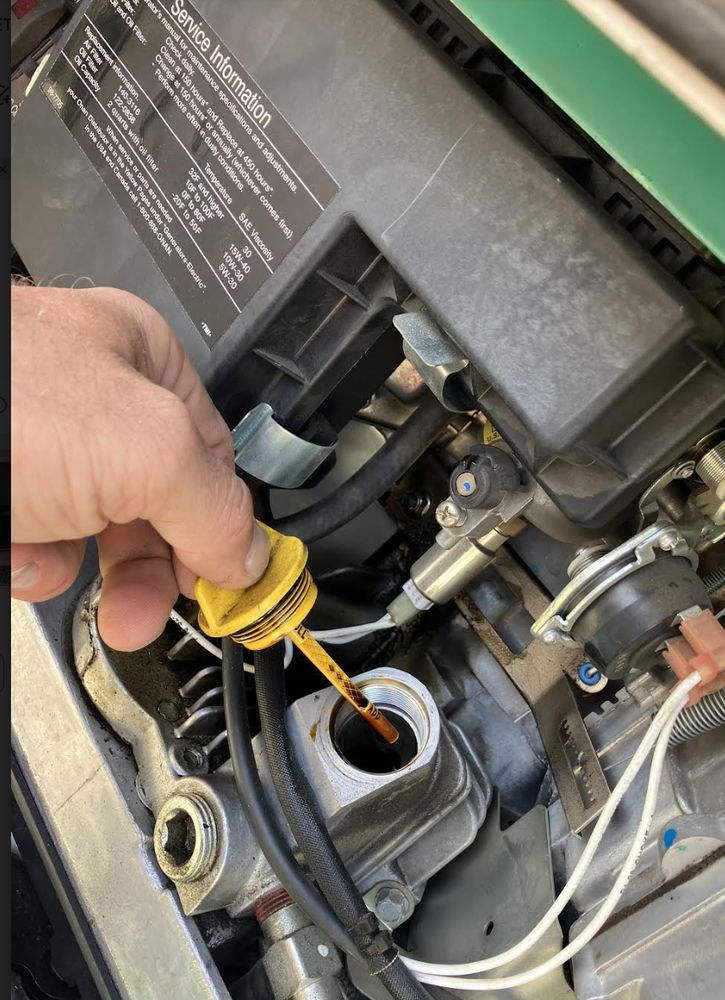 A hand checking the oil level of a generator engine with a yellow dipstick. The engine is in a compartment.