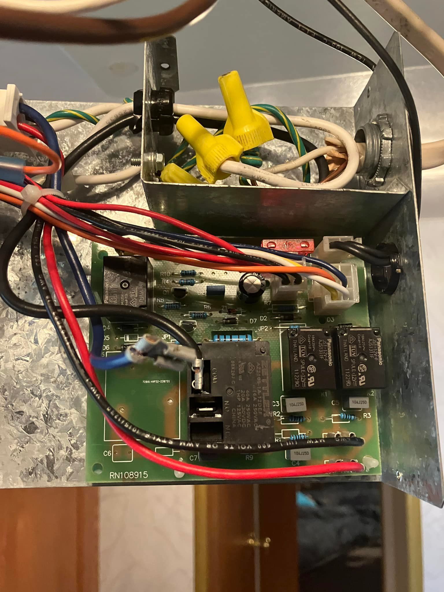 Electronic control board with wires and connectors inside a metal box. Wires are various colors, with yellow wire connectors.