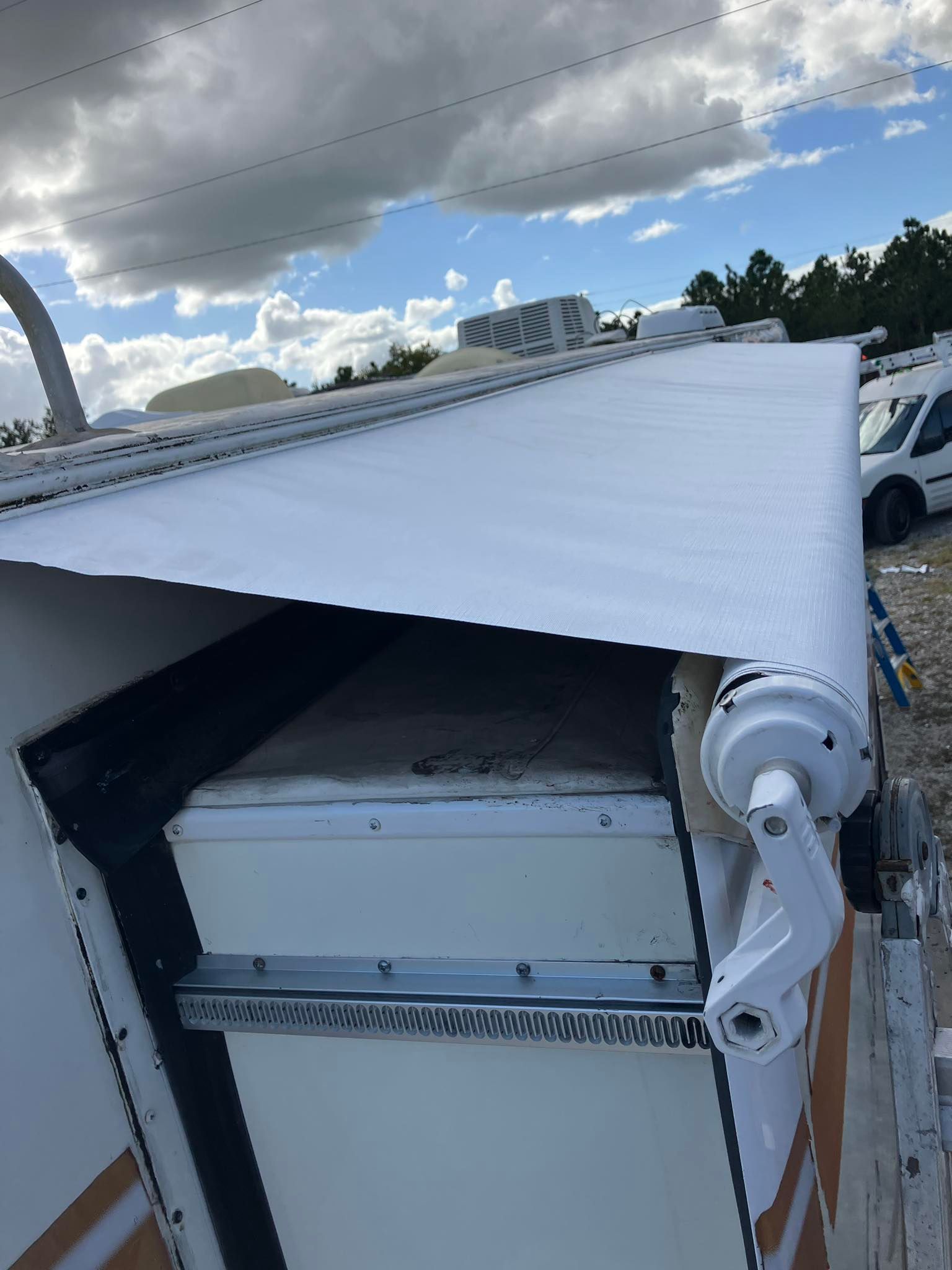 A partially extended white RV awning with a crank mechanism, set against a cloudy sky.