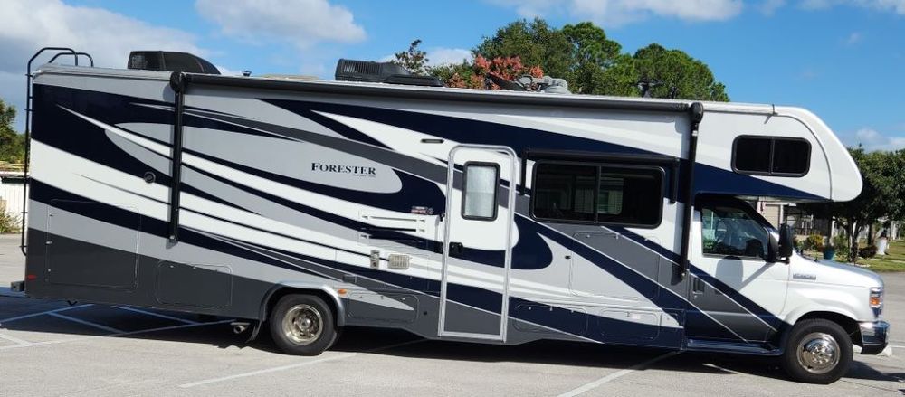 A large, gray and navy blue recreational vehicle parked outside. It has an extended awning and a white front end.