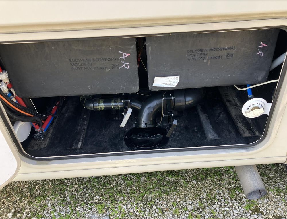 A compartment in a recreational vehicle showing two black tanks, black plumbing, and water lines.