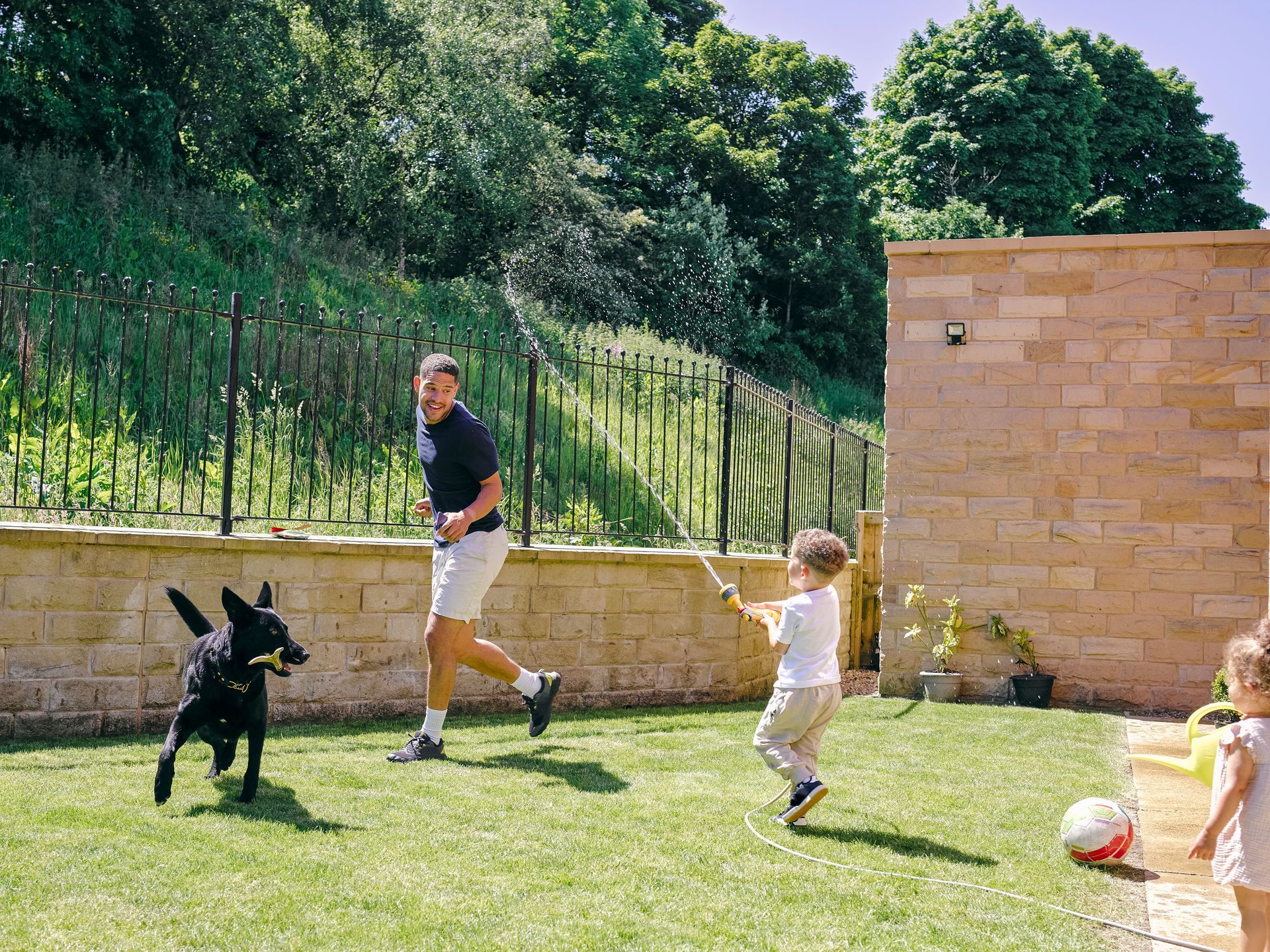 Man and child playing with a dog in a sunny backyard.