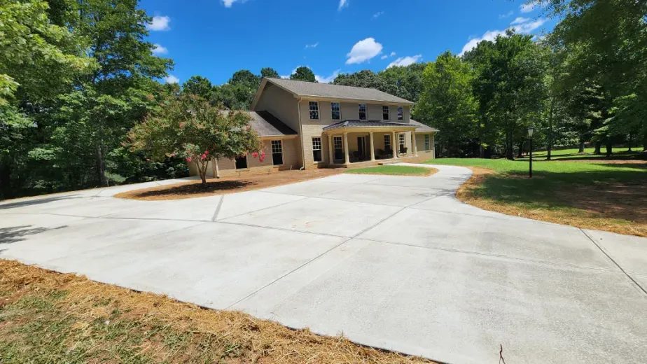 A large house with a concrete driveway leading to it surrounded by trees.