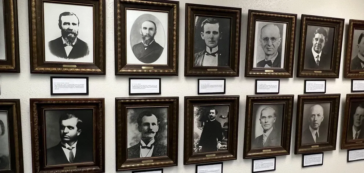 A row of black and white portraits of men are hanging on a wall.