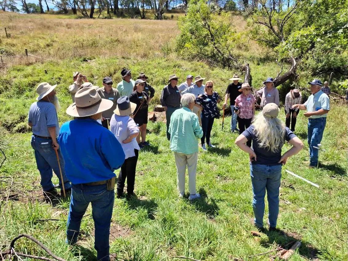 A group of people are standing in a grassy field during an information session.