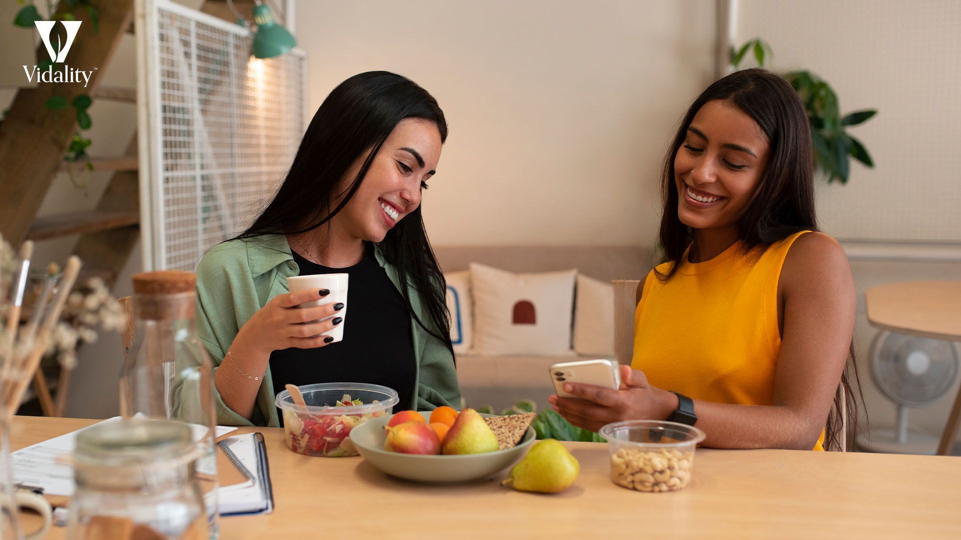 Two women sitting at a table with a bowl of fruit and a cup of coffee.