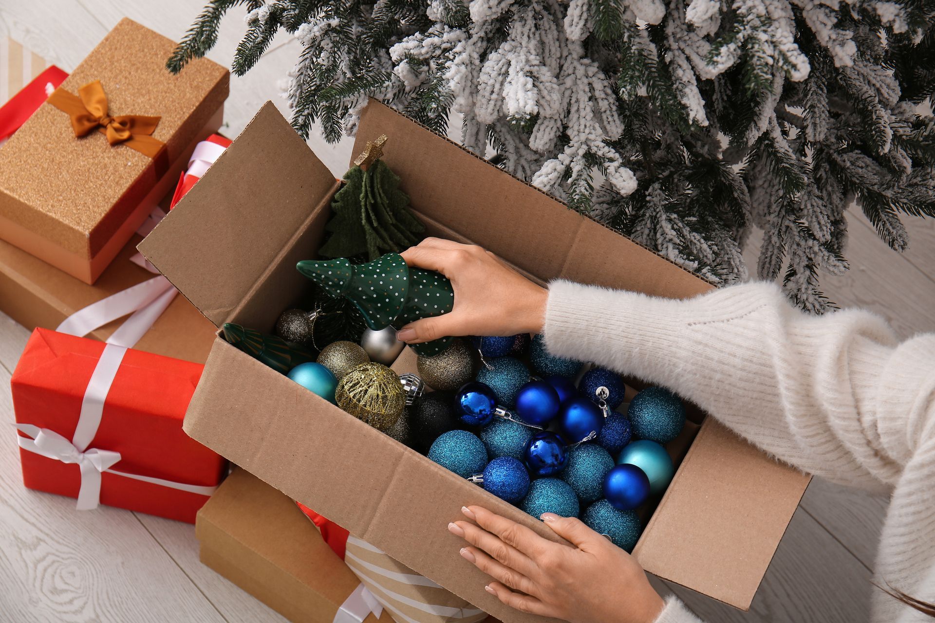 A woman putting Christmas decor in a cardboard box at home, close-up.