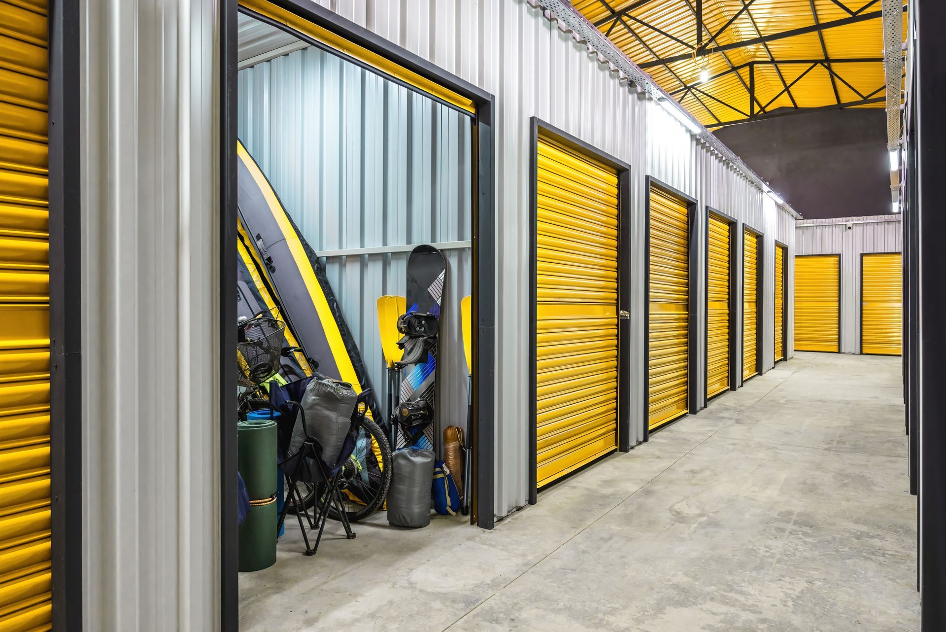 A corridor of self-storage units with yellow doors, with a door open showcasing household storage.