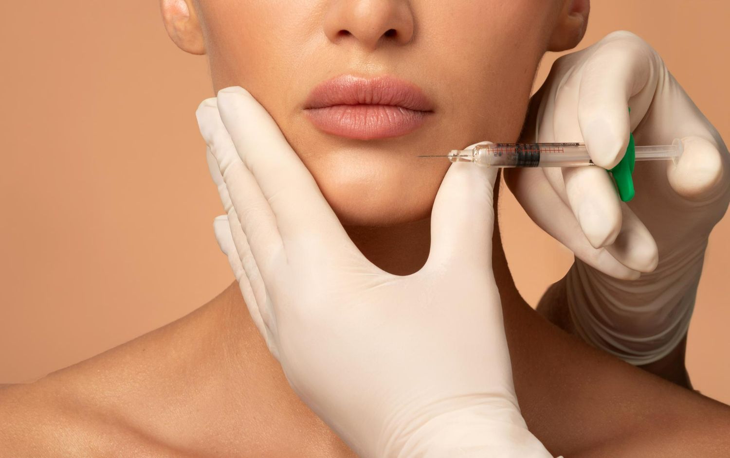 Gloved hands holding a syringe performing a cosmetic injection near a person's lips against a beige background.