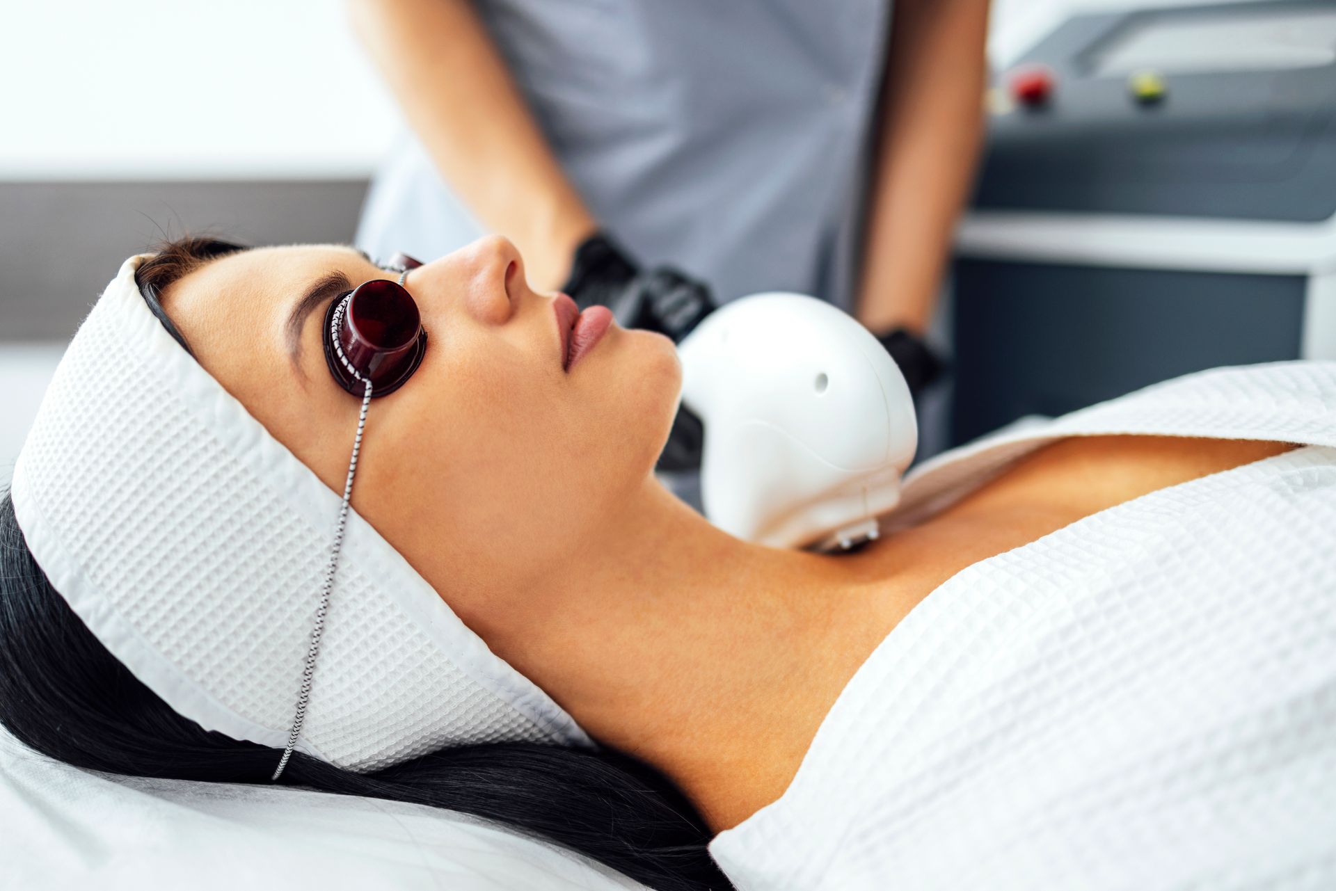 Woman receiving laser treatment on her neck; technician in background.