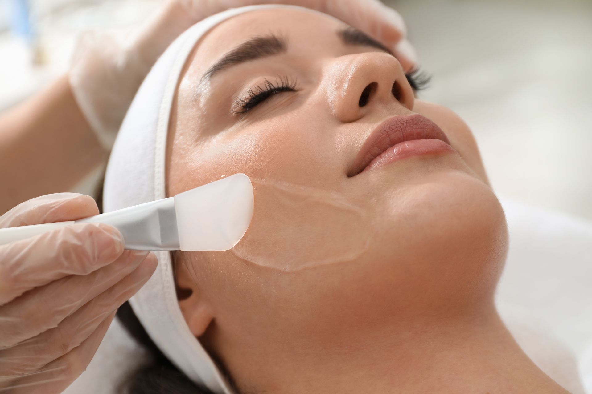 Woman receiving a facial treatment; cosmetician applying a cream with a spatula.