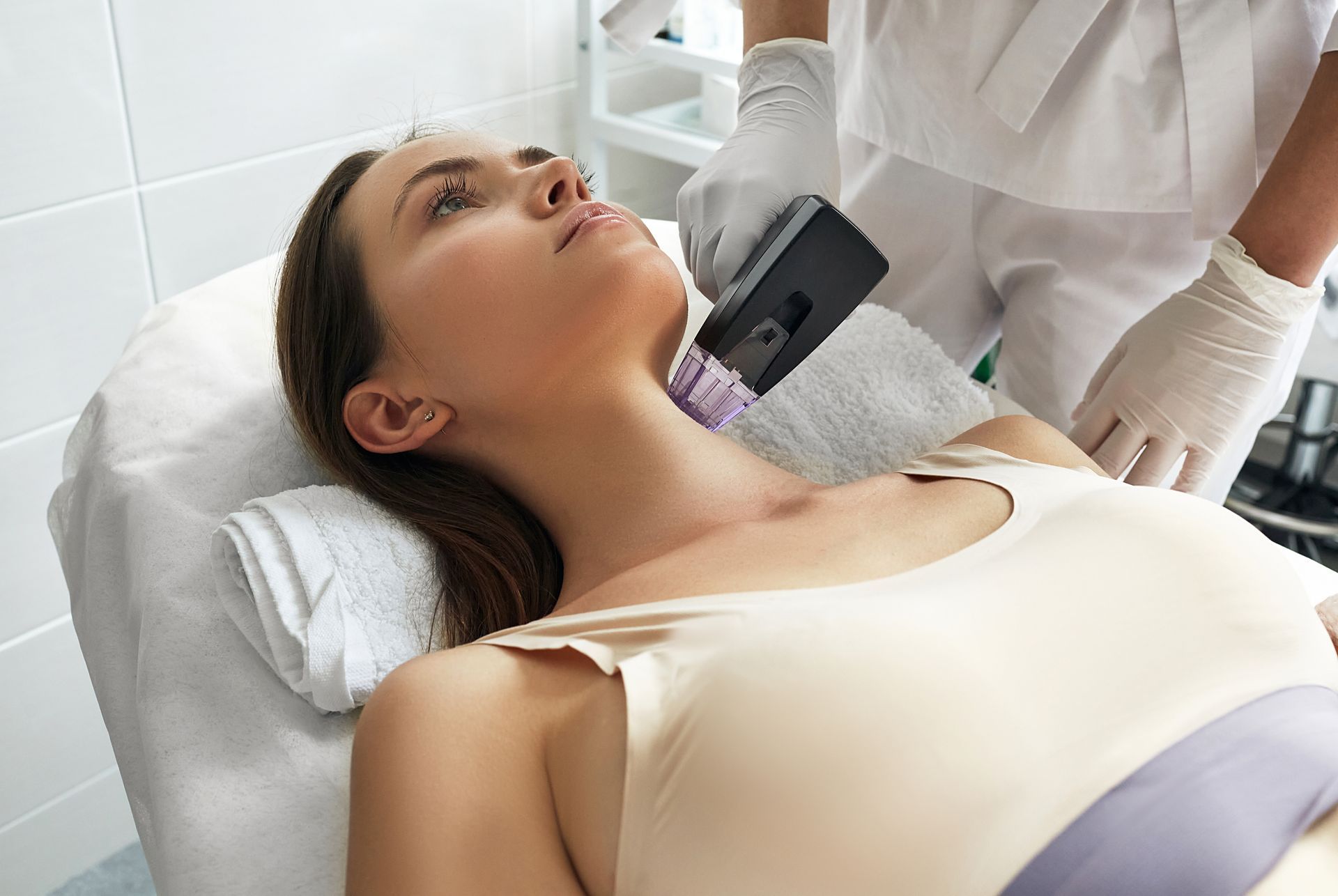 Woman receiving a neck treatment in a clinic; the technician is holding a device.