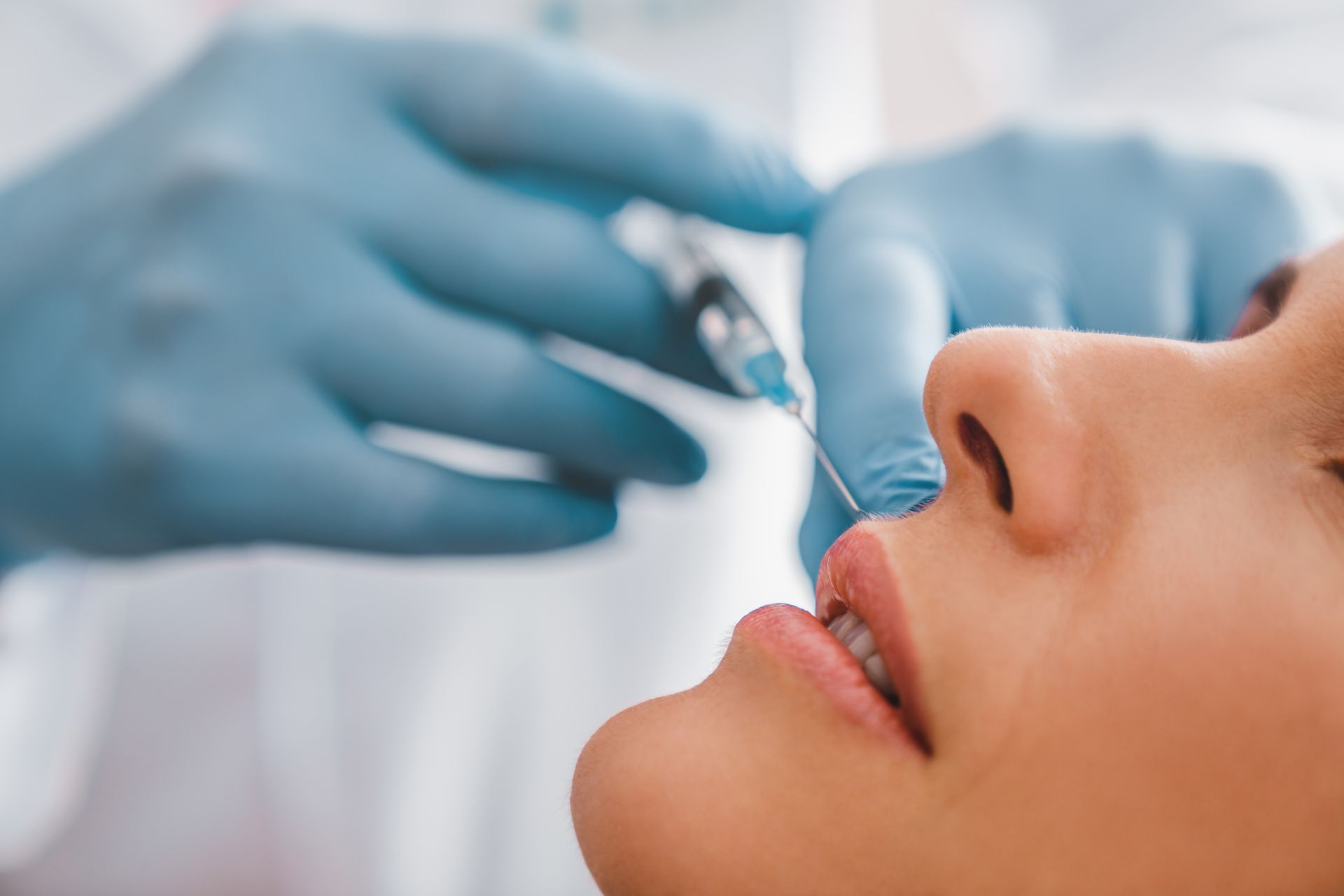 A person receiving a nose injection; gloved hands hold syringe near their nose.