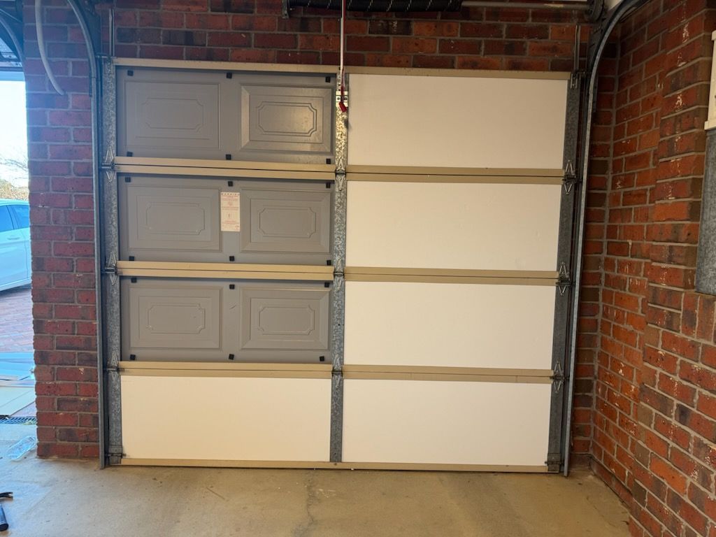 Garage door partially open, showing gray and white panels inside brick building.
