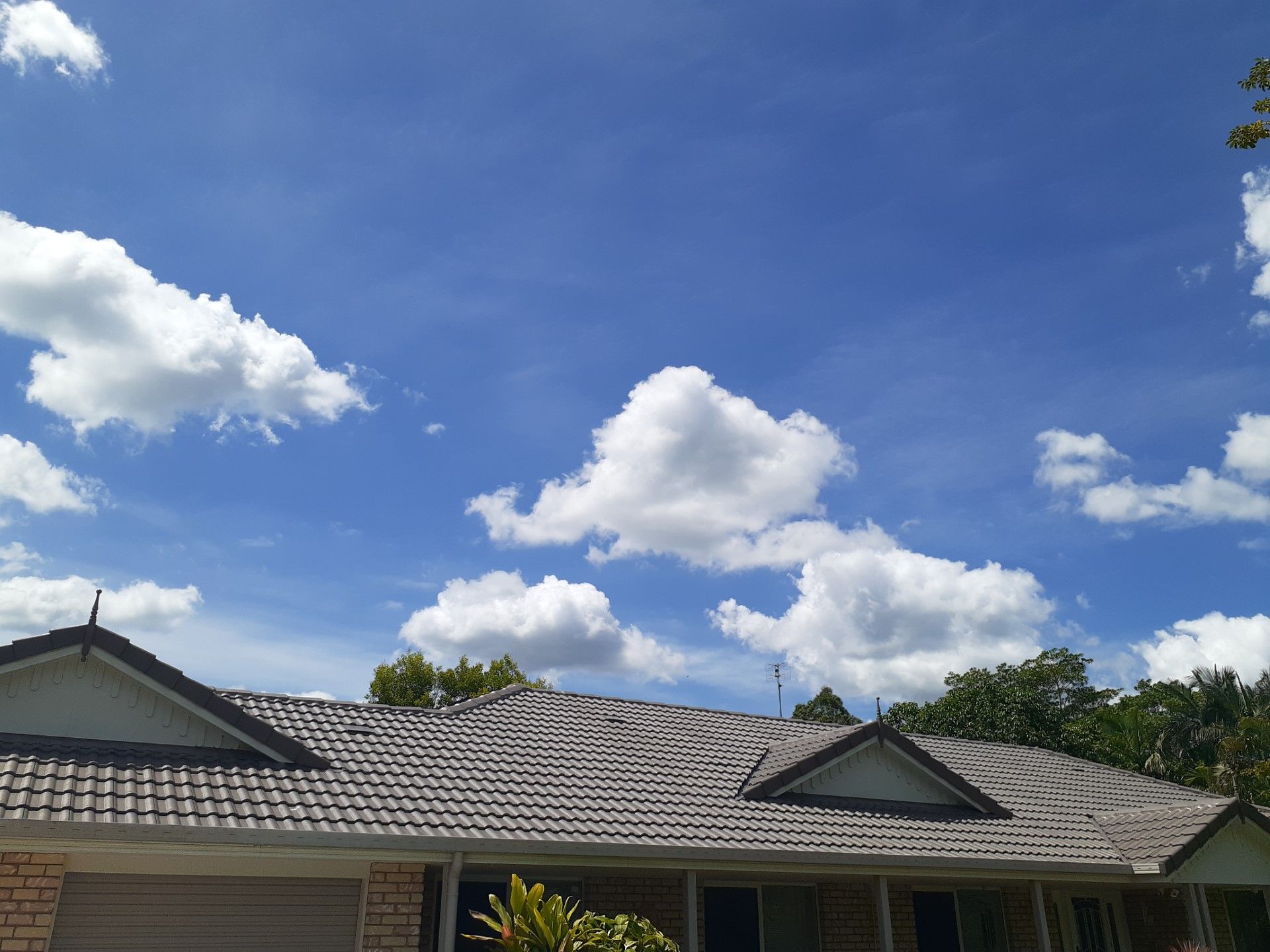 Blue sky with fluffy white clouds above a house with a gray tiled roof.— Vent Wise in Twin Waters, QLD