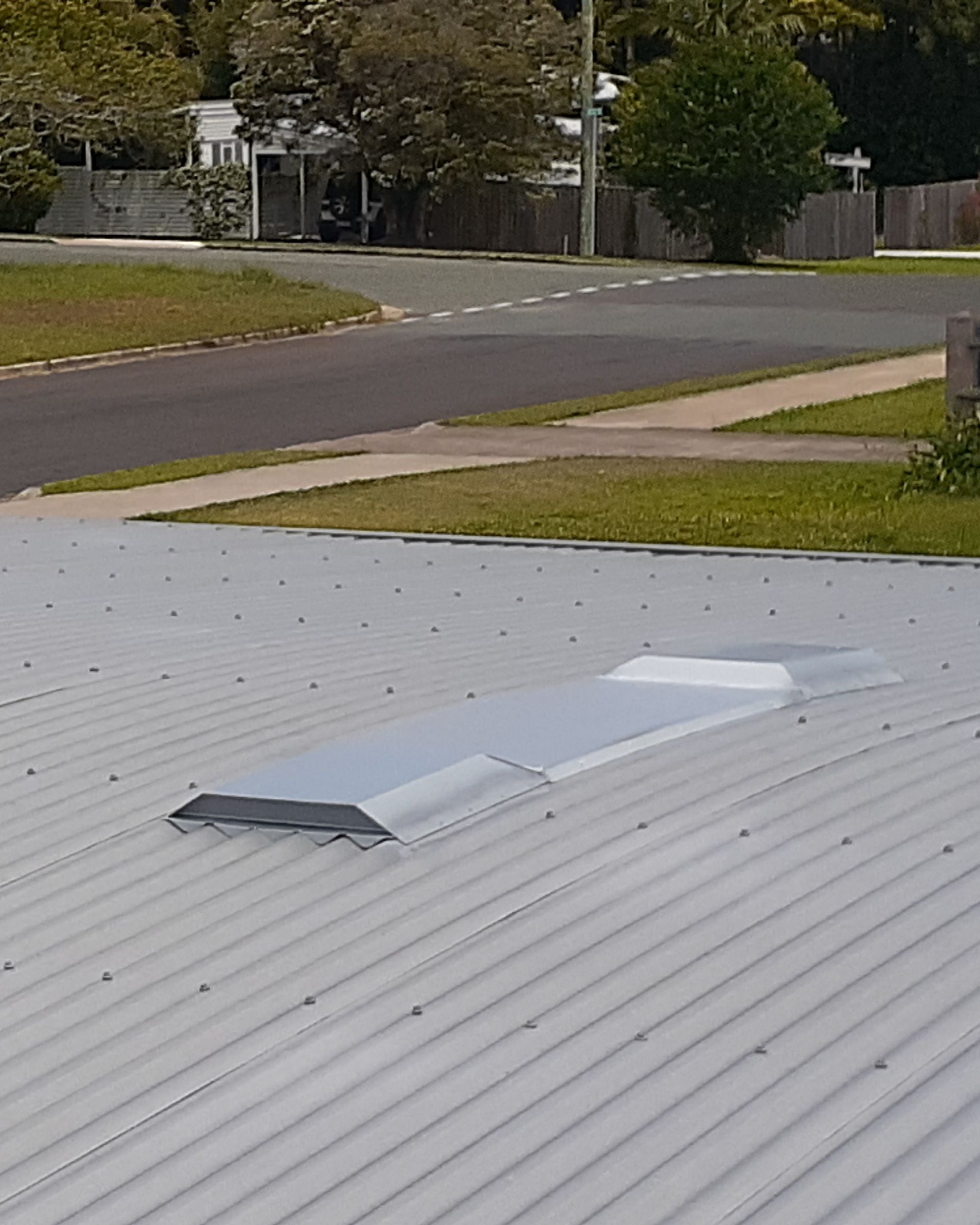 Metal roof with a rectangular skylight, street and greenery in the background. — Vent Wise in Twin Waters, QLD