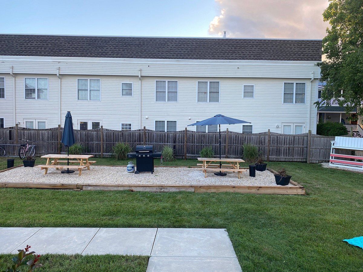 A backyard with a grill and picnic tables in front of a house.