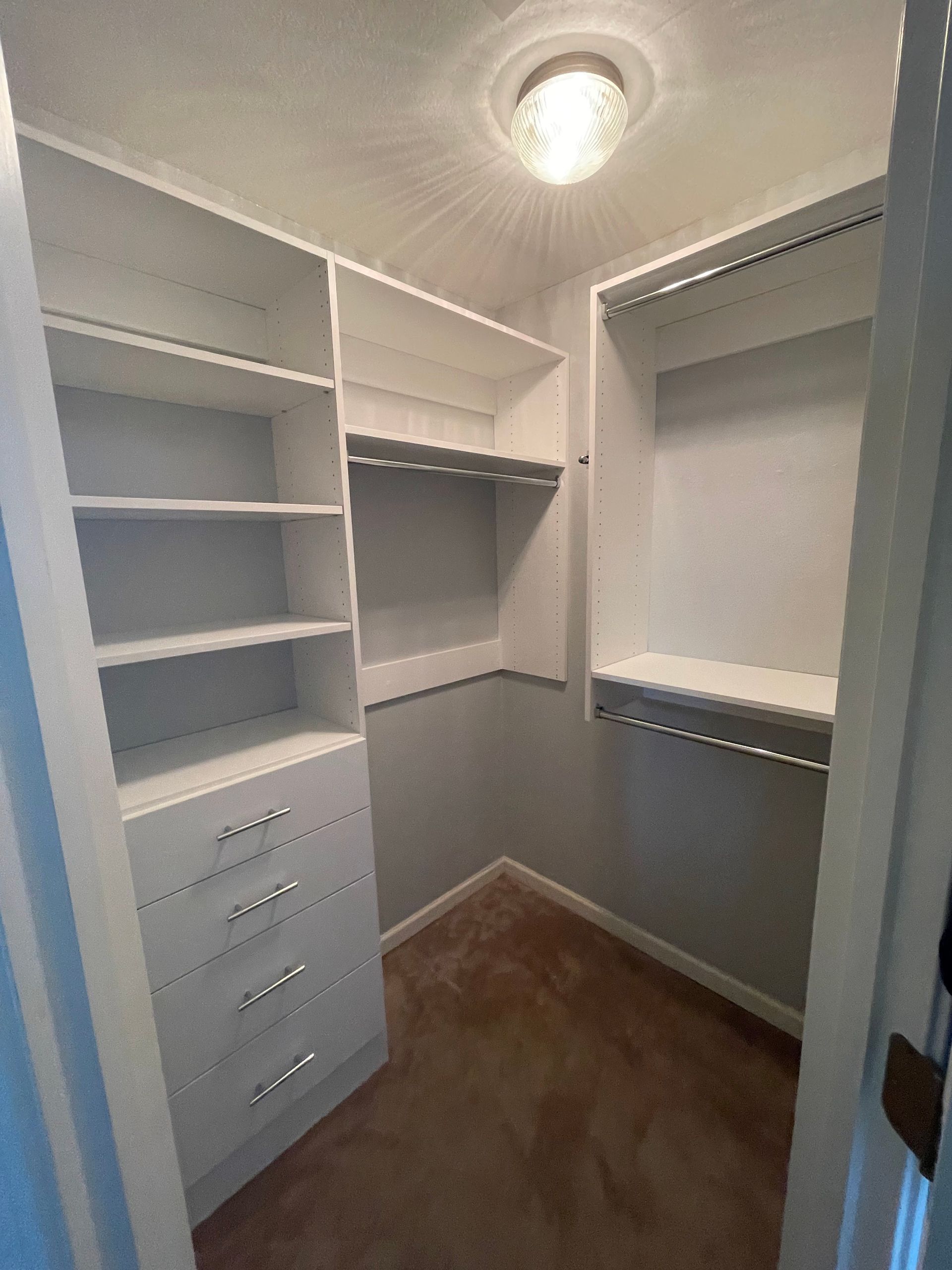 White walk-in closet with built-in shelves and drawers. Beige carpet and a light fixture.
