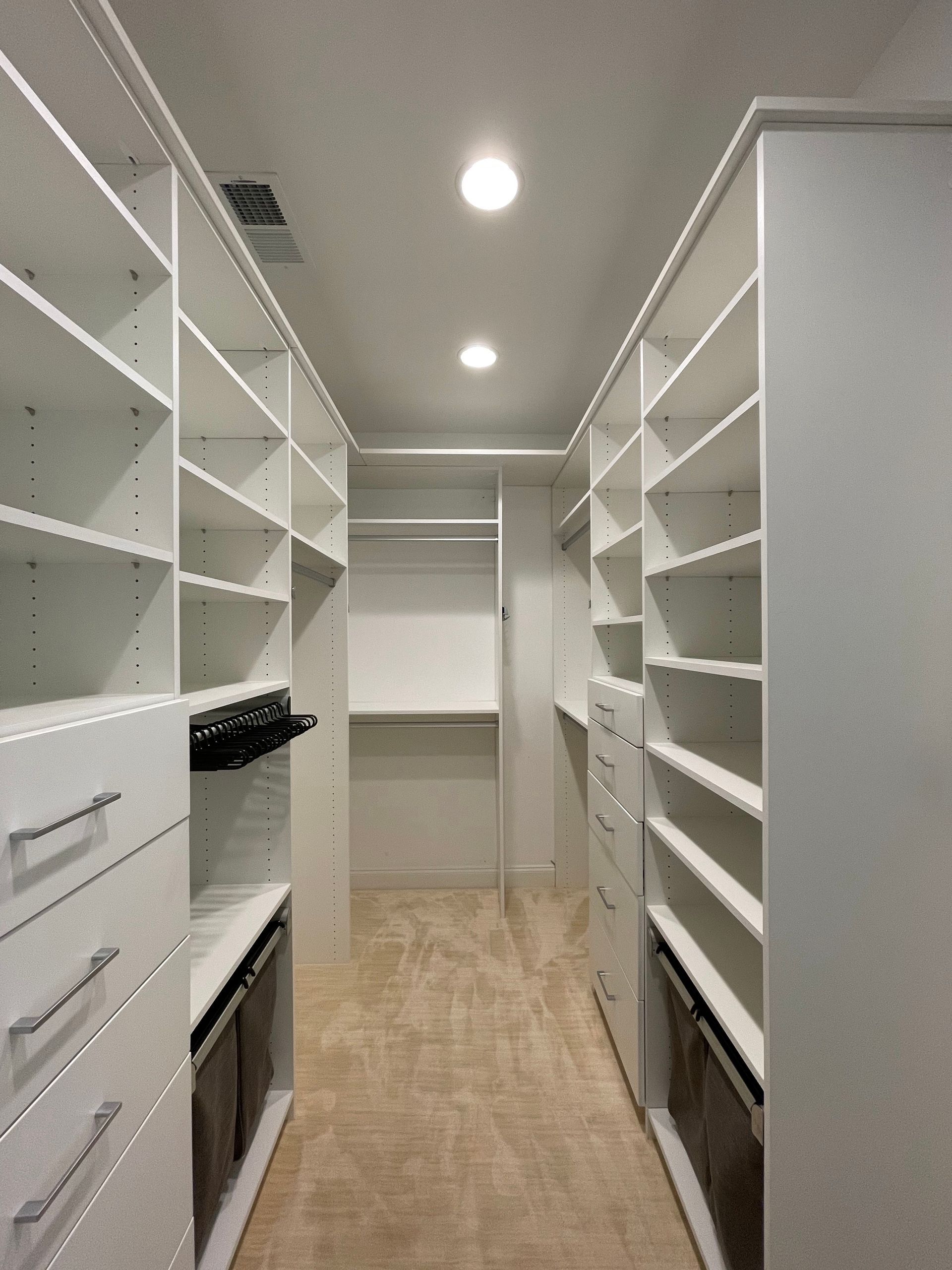 Walk-in closet with white shelving, drawers, and neutral carpet.