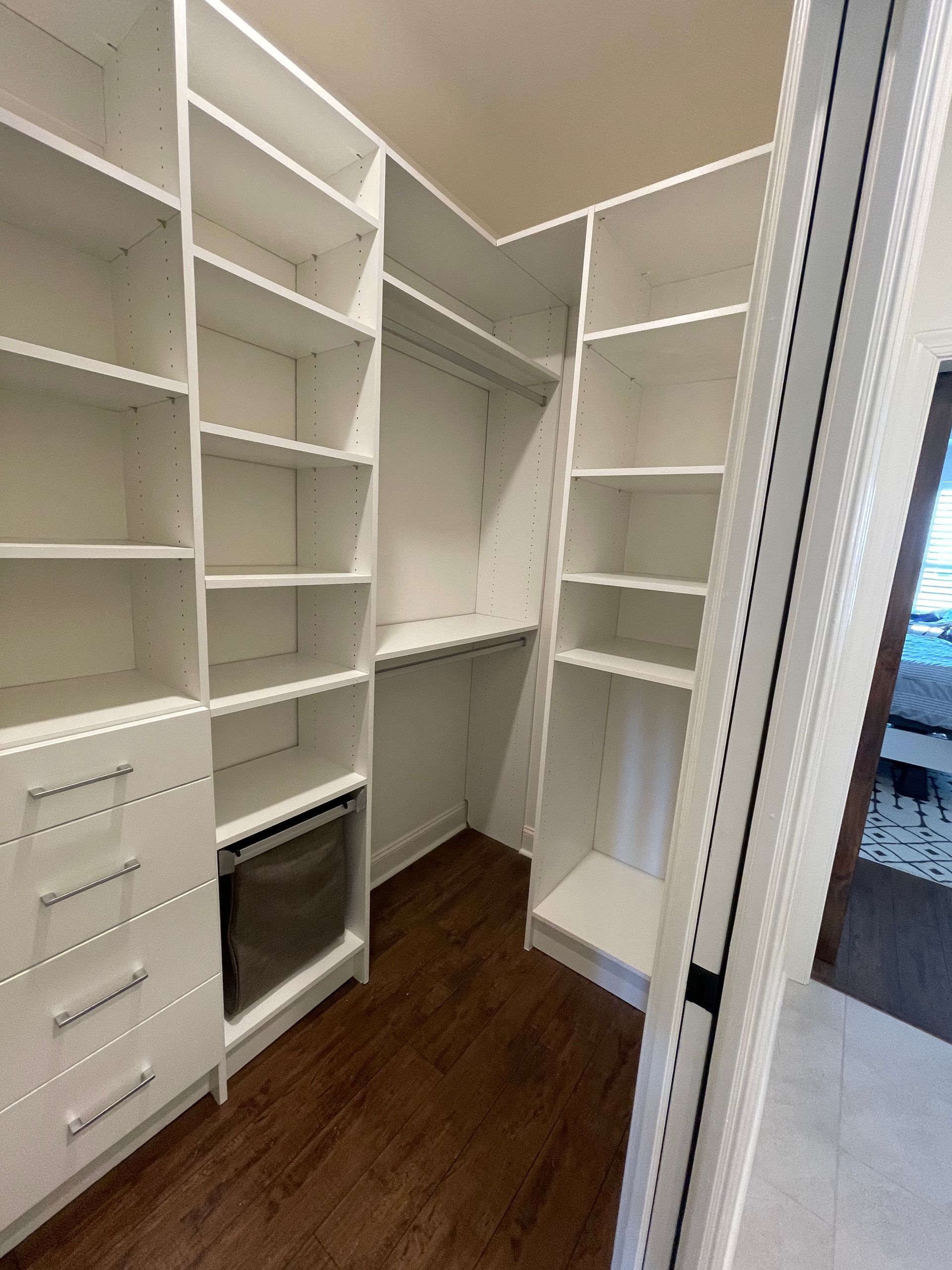 White, custom closet with shelves, drawers, and hanging rod. Dark wood floor.