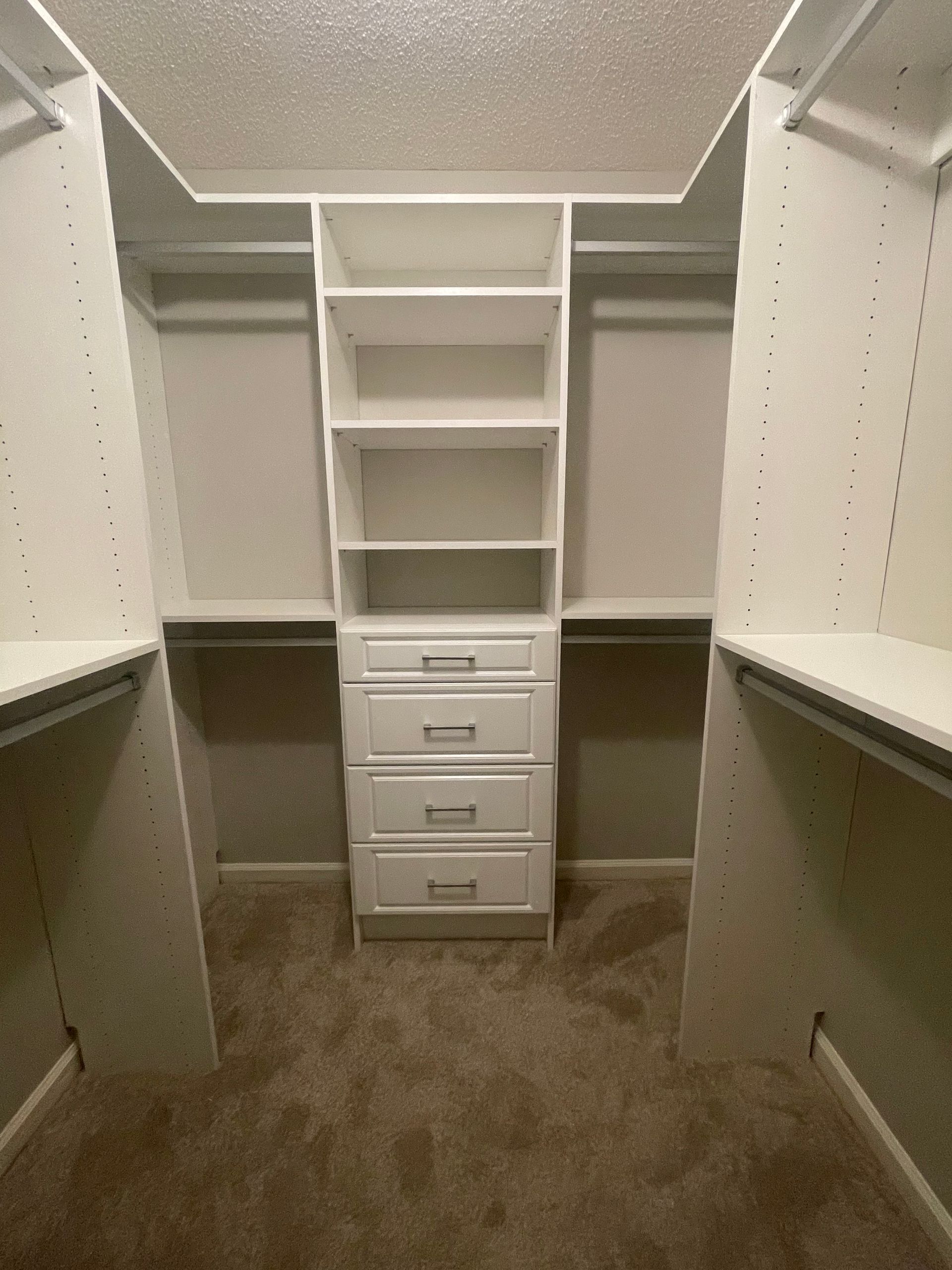 White closet organizer with drawers and shelves in a walk-in closet with brown carpet.