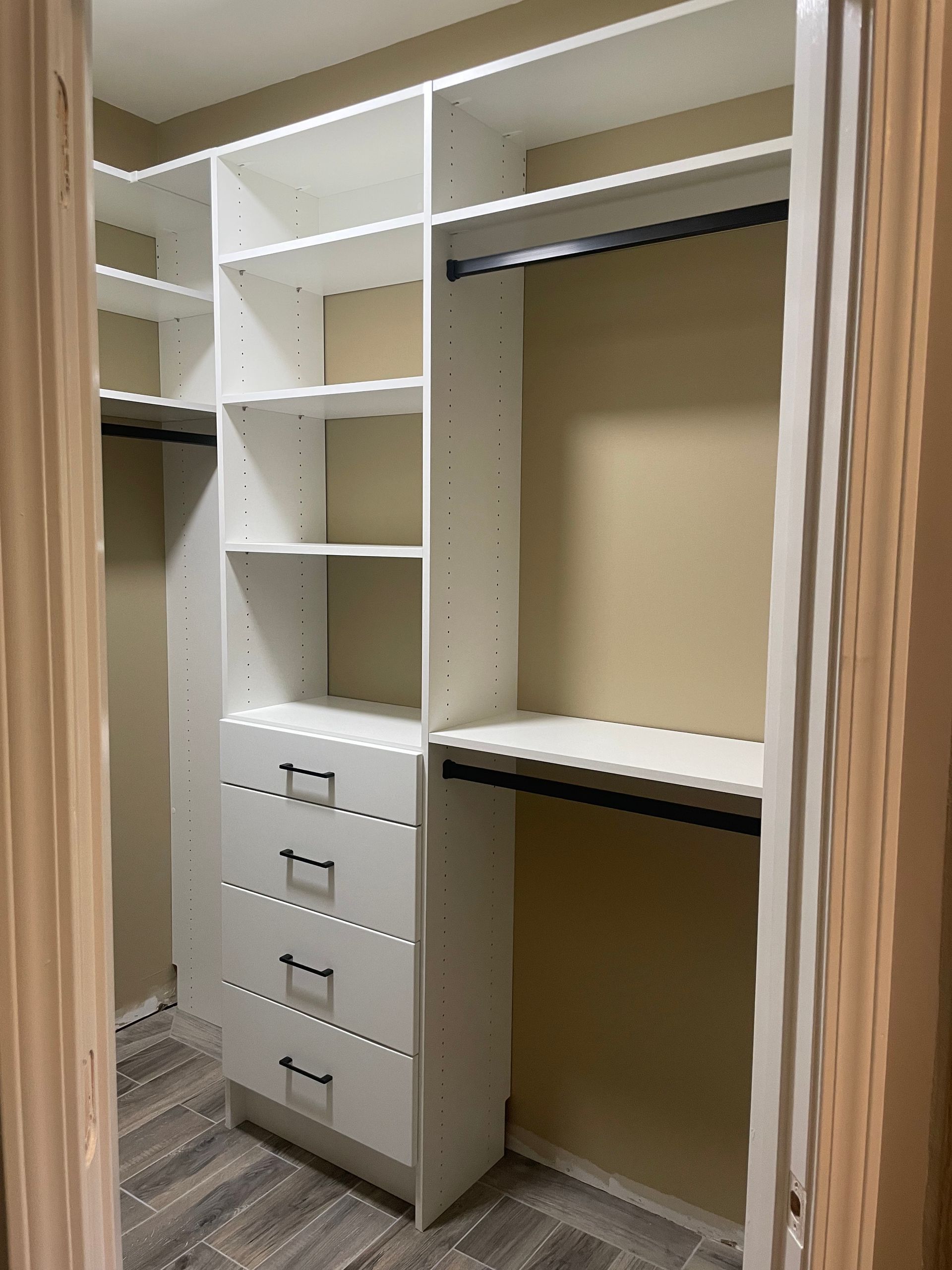 White closet organizer with drawers, shelves, and hanging rods. Beige walls, wood-look floor.
